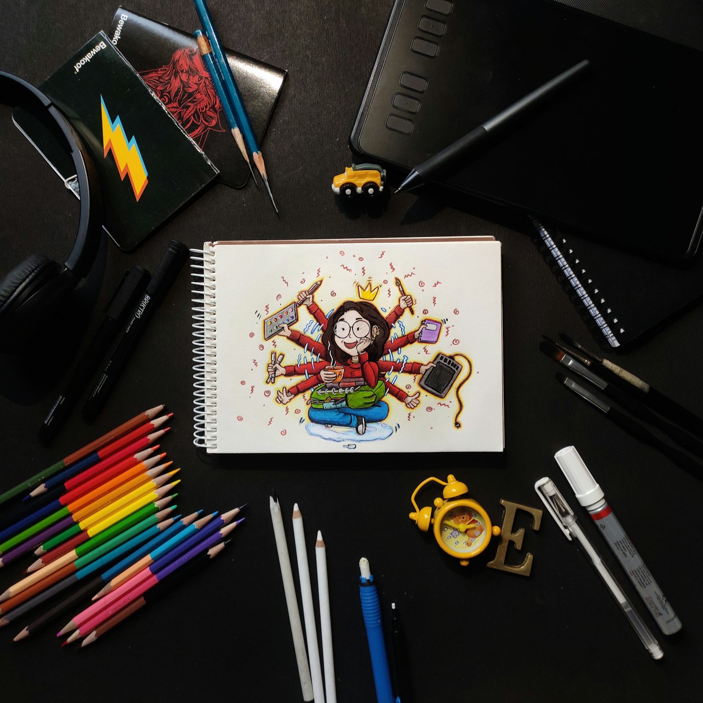 Art supplies and a sketchbook featuring a multitasking woman illustration.